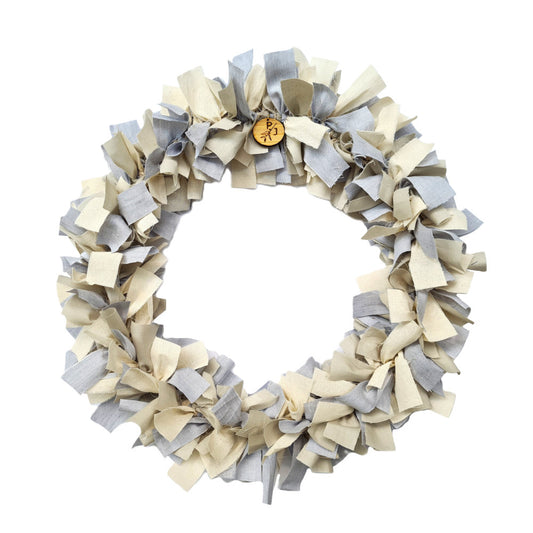 A circular fabric wreath made of layered ruffled strips in light gray and cream, shown on a plain white background.